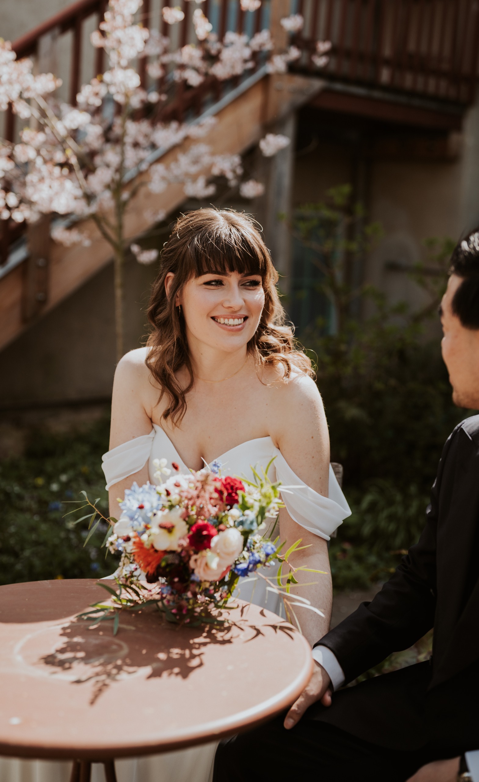 A smiling bride with her bouquet at a café table, in black and white.