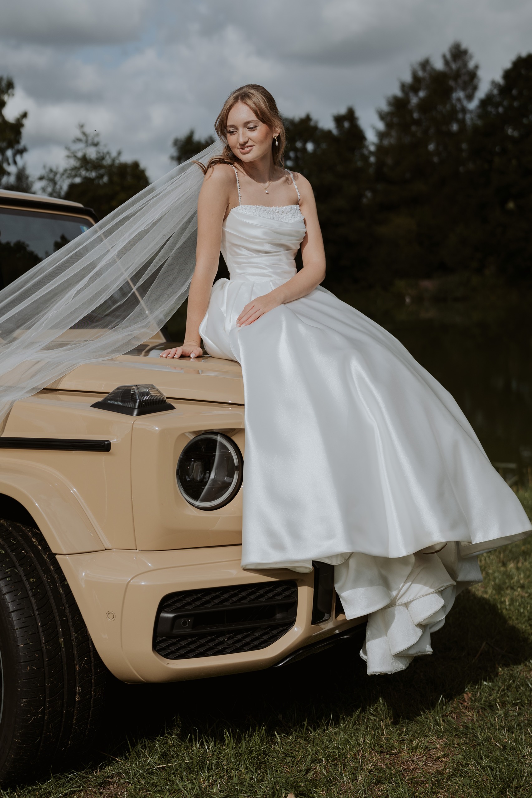 Leonie sitzt mit ihrem fließenden Schleier auf einem Hochzeitsauto.