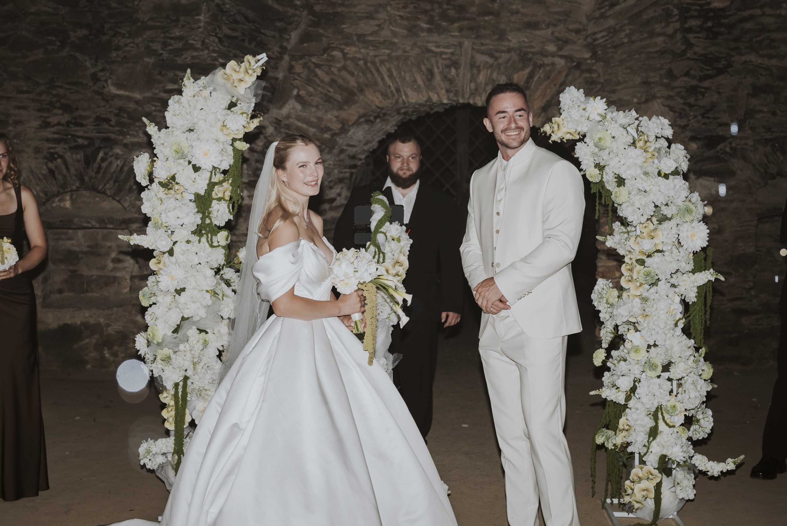 Nadja and Lucas during their ceremony beneath the white floral arch.